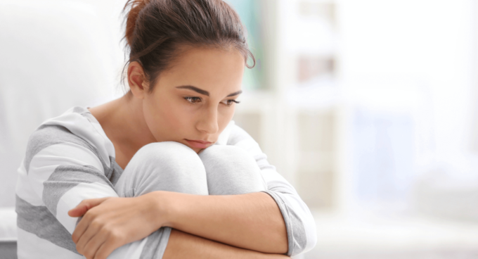 Frau sitzt nachdenklich auf dem Boden und umarmt die Knie