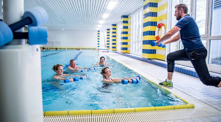 Eine Gruppe macht Sporttherapie im Wasser mit Schaumstoffgewichten in der Hand