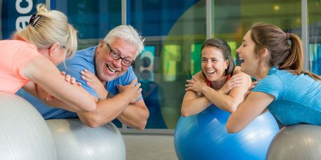 Junge und ältere Menschen freuen sich beim gemeinsamen Übungen auf Pezzibällen