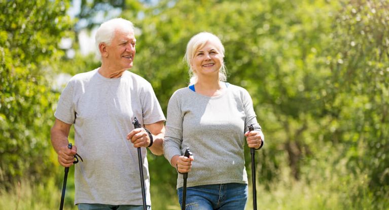 ein älteres Paar spaziert mit Nordic-Walking-Sticks im Wald