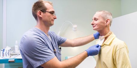 Reha nach Kehlkopfentfernung Ein Arzt untersucht einen Patienten nach der Kehlkopfentfernung