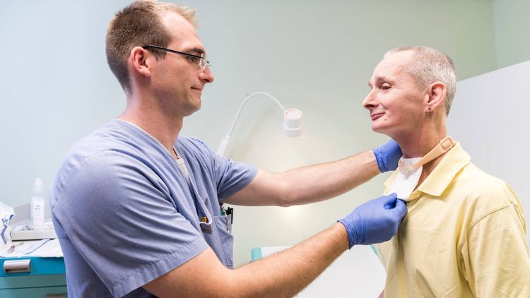 Ein Arzt untersucht einen Patienten nach der Kehlkopfentfernung
