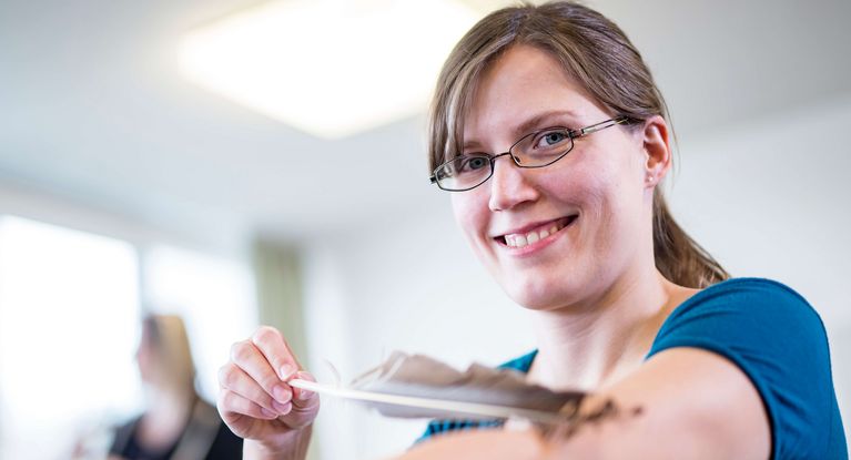 Eine Frau berührt sich mit einer Feder den Arm