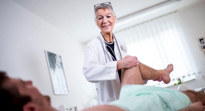 Ärztin untersucht einen Patienten am Knie