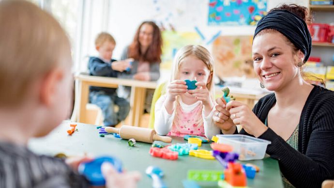 Kinder werden an Tischen mit Spielzeug betreut