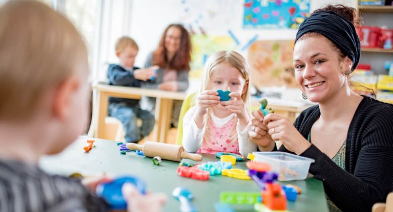 Kinder werden an Tischen mit Spielzeug betreut