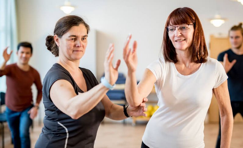 Eine Therapeutin erklärt einer Patienten in der Gruppentherapie eine Tai-Chi-Übung