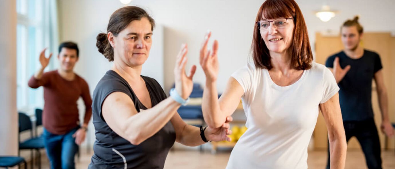 Eine Therapeutin erklärt einer Patienten in der Gruppentherapie eine Tai-Chi-Übung
