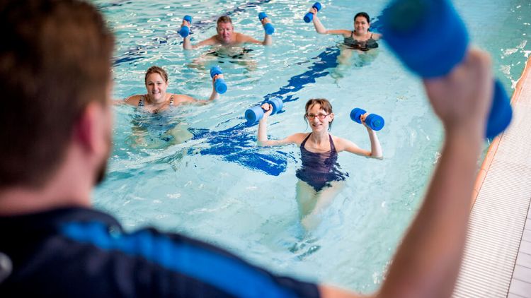 Eine Gruppe macht Sporttherapie im Wasser mit Schaumstoffgewichten in der Hand