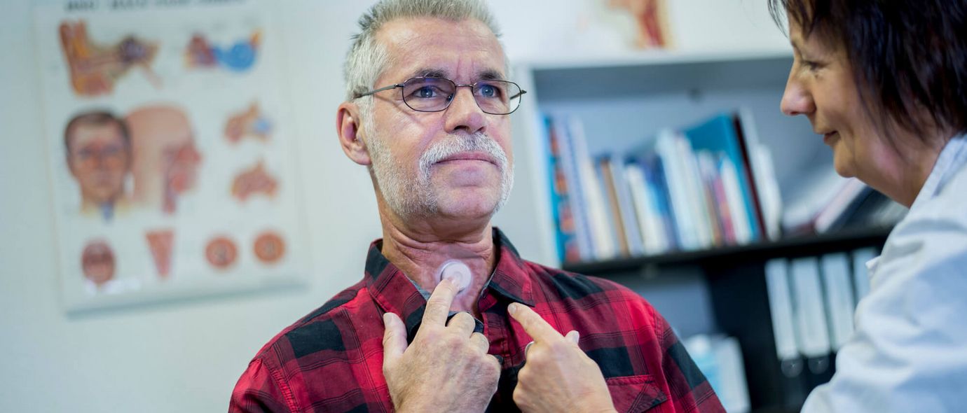 Ärztin zeigt einem Patienten seinen Luftröhrenstoma