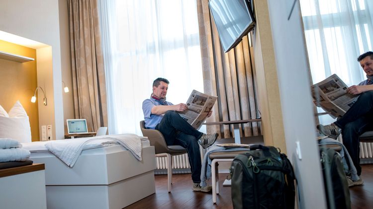 Ein Patient sitzt auf einem Stuhl und liest Zeitung in seinem Patientenzimmer