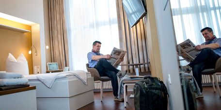 Ein Patient sitzt auf einem Stuhl und liest Zeitung in seinem Patientenzimmer