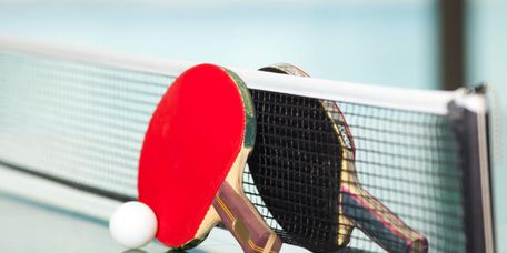 ein roter und ein schwarzer Tischtennisschläger mit einem weißen Ball am Tischtennisnetz auf der Tischtennisplatte