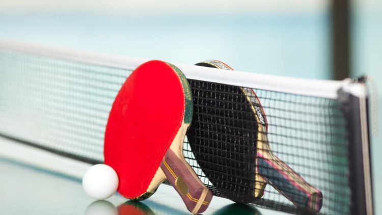 ein roter und ein schwarzer Tischtennisschläger mit einem weißen Ball am Tischtennisnetz auf der Tischtennisplatte