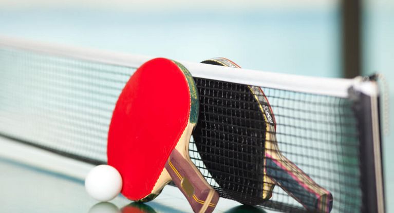 ein roter und ein schwarzer Tischtennisschläger mit einem weißen Ball am Tischtennisnetz auf der Tischtennisplatte