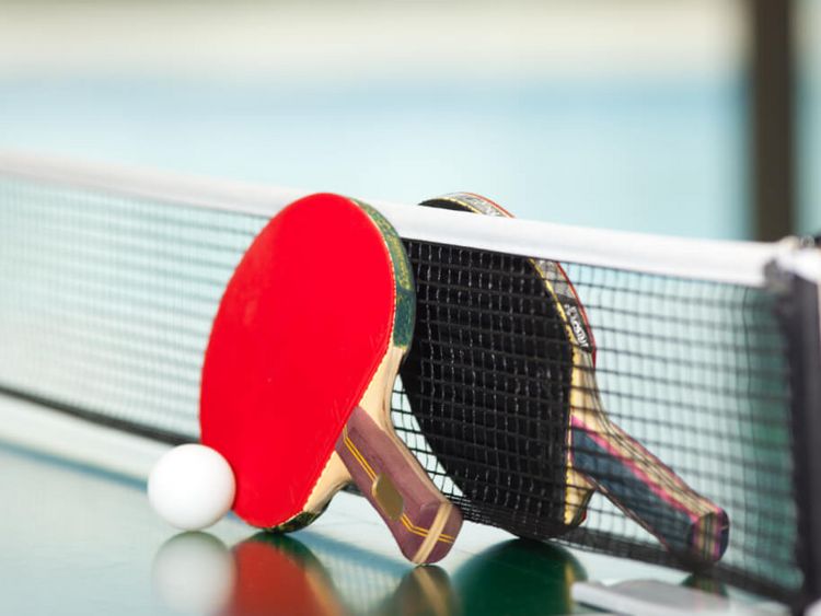 ein roter und ein schwarzer Tischtennisschläger mit einem weißen Ball am Tischtennisnetz auf der Tischtennisplatte